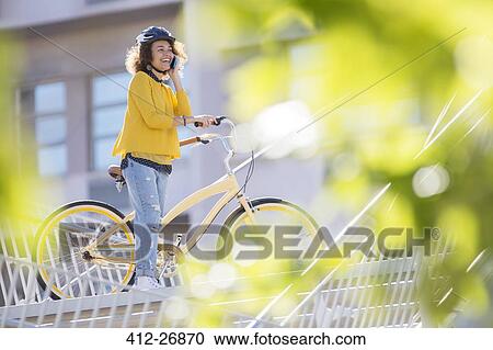 Smiling woman talking on cell phone on bicycle in city View Large Photo Image Stock Image - Smiling woman talking on cell phone on bicycle in city. Fotosearch