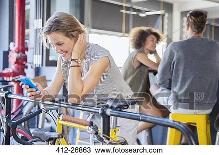 Smiling woman texting with cell phone at railing above bicycle View Large Photo Image Stock Image - Smiling woman texting with cell phone at railing above bicycle. Fotosearch