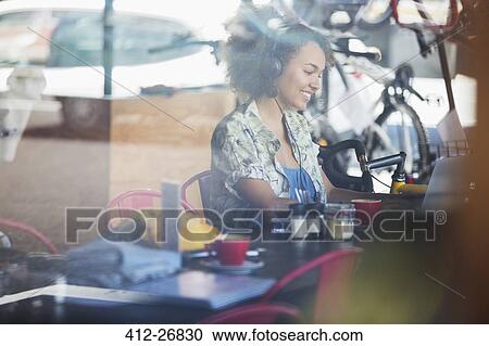 Smiling woman with headphones at laptop in cafe View Large Photo Image Stock Image - Smiling woman with headphones at laptop in cafe. Fotosearch