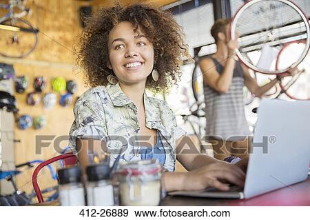 Smiling woman working at laptop in bicycle shop View Large Photo Image Stock Photo - Smiling woman working at laptop in bicycle shop. Fotosearch