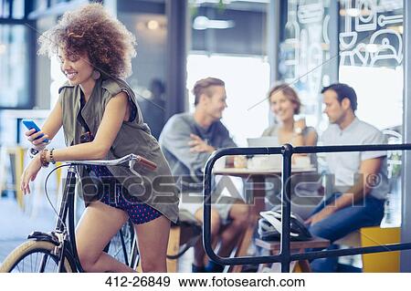 Woman on bicycle texting with cell phone at cafe View Large Photo Image Stock Photo - Woman on bicycle texting with cell phone at cafe. Fotosearch