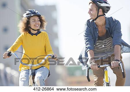 Young couple with helmets riding bicycles in city View Large Photo Image Picture - Young couple with helmets riding bicycles in city. Fotosearch