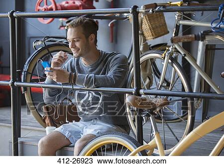 Stock Image - Young man texting with cell phone near bicycles at railing. Fotosearch