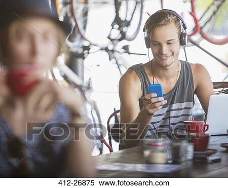 Young man with headphones and laptop texting with cell phone in cafe View Large Photo Image Stock Photography - Young man with headphones and laptop texting with cell phone in cafe. Fotosearch