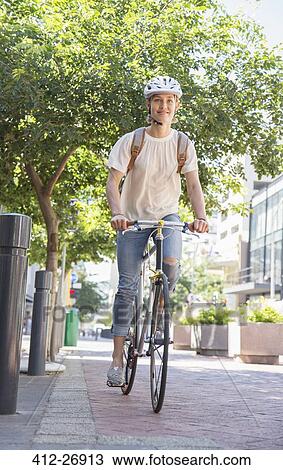 Stock Image - Young woman with helmet riding bicycle in urban park. Fotosearch