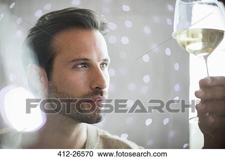 Stock Image - Close up serious man examining white wine. Fotosearch