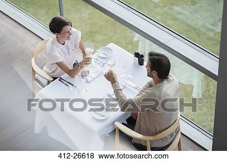 Couple toasting wine glasses at restaurant table at window View Large Photo Image Stock Photo - Couple toasting wine glasses at restaurant table at window. Fotosearch