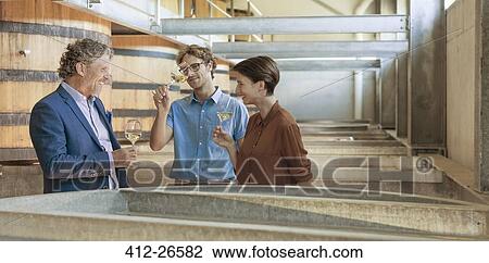 Stock Image - Friends barrel tasting wine in winery cellar. Fotosearch