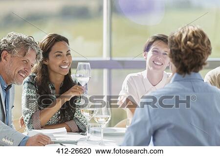 Stock Image - Friends drinking wine and talking at restaurant table. Fotosearch