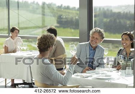 Stock Image - Friends drinking wine and talking in winery dining room. Fotosearch