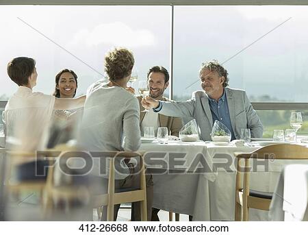 Friends toasting wine glasses at sunny restaurant table View Large Photo Image Stock Photo - Friends toasting wine glasses at sunny restaurant table. Fotosearch