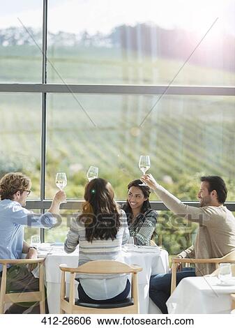 Friends toasting wine glasses in winery dining room View Large Photo Image Stock Photograph - Friends toasting wine glasses in winery dining room. Fotosearch