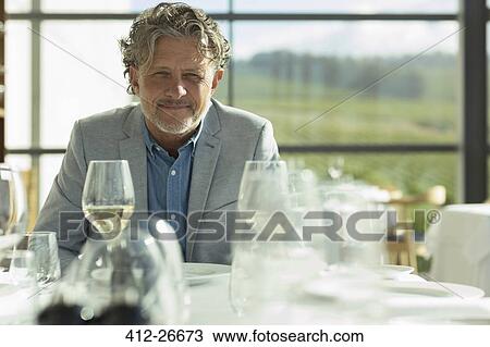 Stock Image - Portrait confident man with white wine at sunny restaurant table. Fotosearch