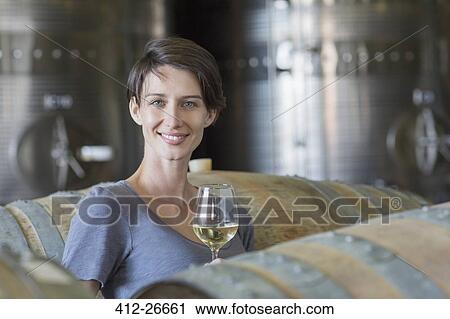Stock Image - Portrait confident vintner drinking white wine in winery cellar. Fotosearch