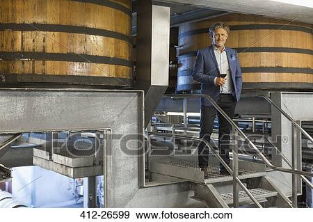 Stock Photo - Portrait confident vintner with red wine on platform in winery cellar. Fotosearch