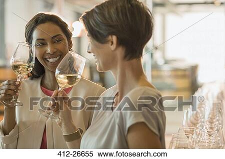 Stock Photography - Smiling women wine tasting white wine in winery tasting room. Fotosearch