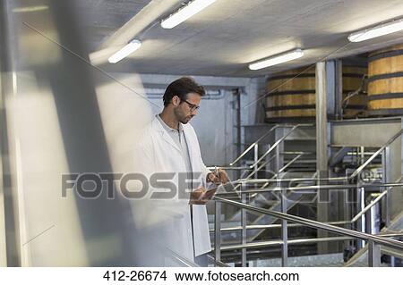 Vintner in lab coat with clipboard in winery cellar View Large Photo Image Picture - Vintner in lab coat with clipboard in winery cellar. Fotosearch