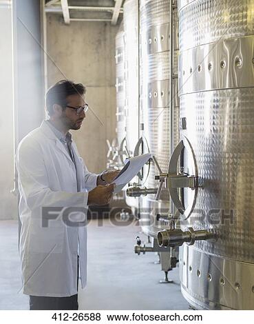 Vintner in lab coat with clipboard checking stainless steel vat in winery cellar View Large Photo Image Stock Photo - Vintner in lab coat with clipboard checking stainless steel vat in winery cellar. Fotosearch