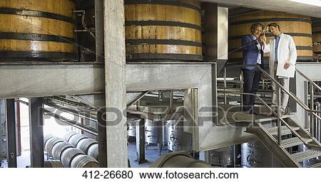 Stock Image - Vintners examining wine on platform in winery cellar. Fotosearch
