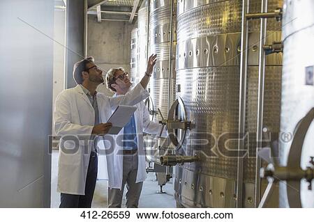 Stock Photo - Vintners in lab coats checking vats in winery cellar. Fotosearch