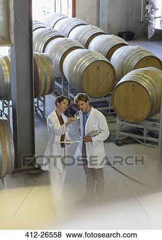 Vintners in lab coats examining wine in winery cellar View Large Photo Image Stock Photo - Vintners in lab coats examining wine in winery cellar. Fotosearch