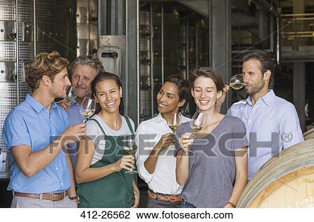 Stock Image - Winery employees tasting white wine in cellar. Fotosearch