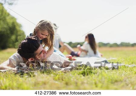 Affectionate daughter laying on top of father in sunny field View Large Photo Image Stock Photograph - Affectionate daughter laying on top of father in sunny field. Fotosearch