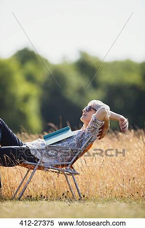 Carefree senior woman relaxing with book in sunny field View Large Photo Image Stock Photography - Carefree senior woman relaxing with book in sunny field. Fotosearch