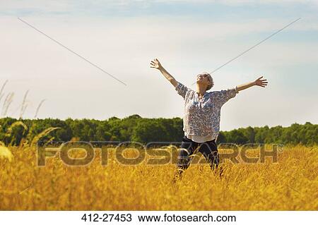 Stock Image - Exuberant senior woman with arms outstretched in sunny rural field. Fotosearch