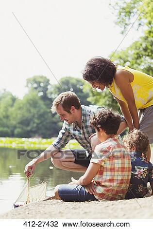 Family playing with toy sailboat at lakeside View Large Photo Image Stock Image - Family playing with toy sailboat at lakeside. Fotosearch