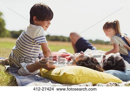 Picture - Family relaxing on blanket in sunny field. Fotosearch
