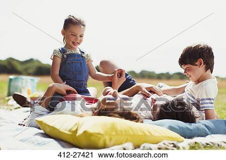 Stock Image - Family relaxing on blanket in sunny field. Fotosearch