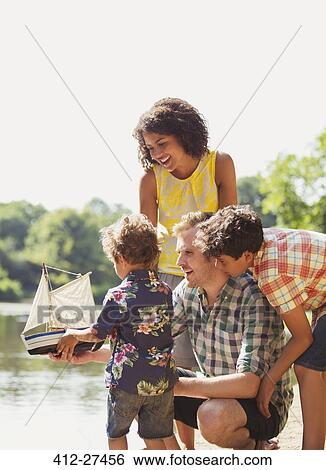 Family with toy sailboat at sunny lakeside View Large Photo Image Stock Photograph - Family with toy sailboat at sunny lakeside. Fotosearch
