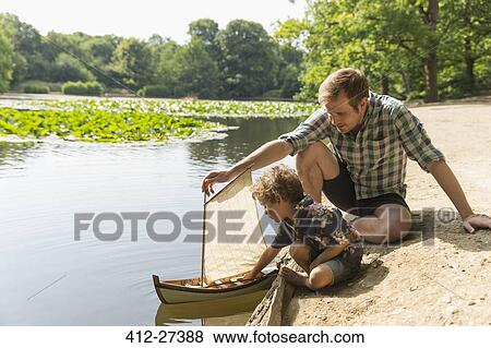 Father and son playing with toy sailboat at lakeside View Large Photo Image Stock Photo - Father and son playing with toy sailboat at lakeside. Fotosearch