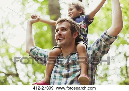 Stock Photo - Father carrying son on shoulders below trees. Fotosearch