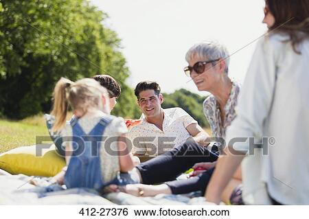 Stock Photograph - Multi-generation family relaxing on blanket in sunny field. Fotosearch