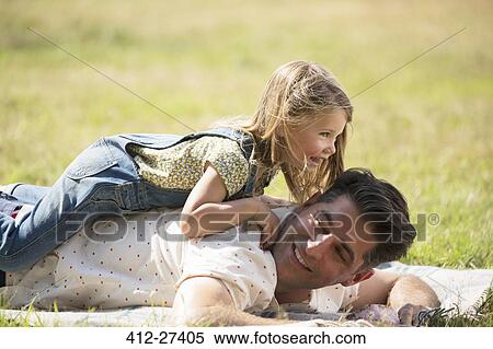 Playful daughter laying on top of father in sunny field View Large Photo Image Stock Photography - Playful daughter laying on top of father in sunny field. Fotosearch