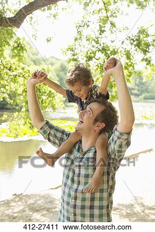 Playful father carrying son on shoulders at lakeside View Large Photo Image Stock Image - Playful father carrying son on shoulders at lakeside. Fotosearch