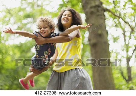 Playful mother flying son under tree View Large Photo Image Stock Photograph - Playful mother flying son under tree. Fotosearch