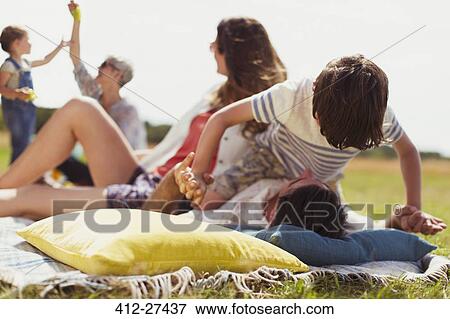 Stock Photo - Playful son balancing on top of father in sunny field. Fotosearch