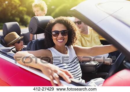 Stock Photo - Portrait enthusiastic woman driving convertible with family. Fotosearch