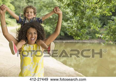 Stock Photo - Portrait playful mother carrying son on shoulders near pond. Fotosearch