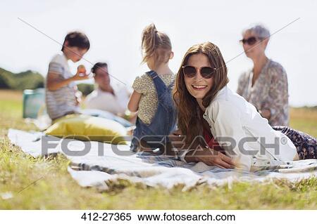 Portrait smiling woman laying on blanket in sunny field with family View Large Photo Image Stock Photography - Portrait smiling woman laying on blanket in sunny field with family. Fotosearch