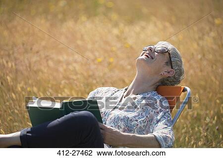 Senior woman reading book and laughing with head back in sunny field View Large Photo Image Stock Image - Senior woman reading book and laughing with head back in sunny field. Fotosearch