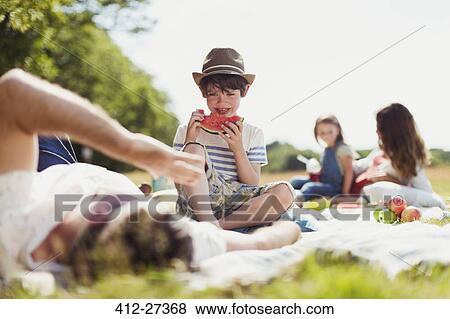 Smiling boy eating watermelon on blanket in sunny field View Large Photo Image Stock Photo - Smiling boy eating watermelon on blanket in sunny field. Fotosearch