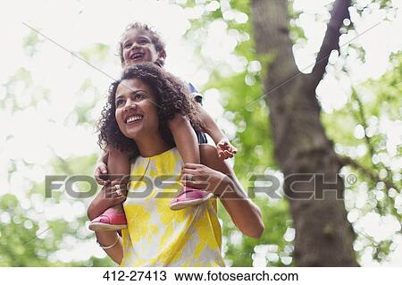 Smiling mother carrying son on shoulders below tree View Large Photo Image Stock Image - Smiling mother carrying son on shoulders below tree. Fotosearch
