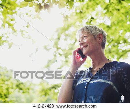 Smiling senior woman talking on cell phone below trees View Large Photo Image Stock Photo - Smiling senior woman talking on cell phone below trees. Fotosearch