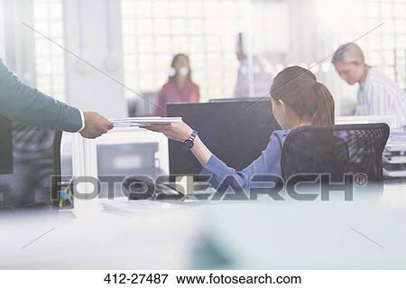 Stock Photo - Businessman handing paperwork to businesswoman at desk. Fotosearch
