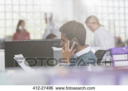Businessman with paperwork talking on cell phone in office View Large Photo Image Stock Photograph - Businessman with paperwork talking on cell phone in office. Fotosearch