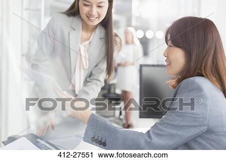 Stock Image - Businesswomen discussing paperwork in office. Fotosearch